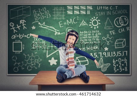 Portrait of cheerful boy flying on the table while wearing helmet and scarf with doodle background on the chalkboard