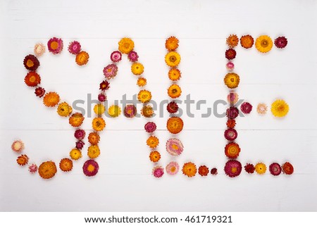 Top view of a word sale made by flower heads over white plank background