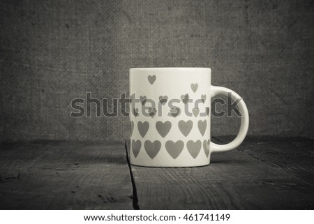 Mug with many pictured hearts on the old wooden table. Toned.