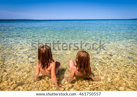 Children on Beach in Croatia island Pag or Hvar.  Twins sitting in Turquoise and blue sea water of Adriatic and Mediterranean sea. Beautiful background landscape photo with calm sea and blue skies.