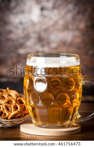 A glass of fresh cold light beer with pretzel and wheat in a bar and a dark pub