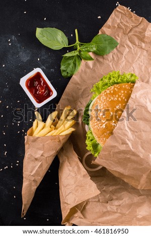 Burger with fries in a paper bag and sauce on a black background.