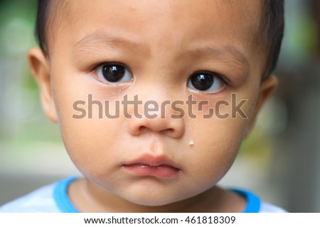 A close up shot of an asian  boy looking at the camera with big round sad eyes 