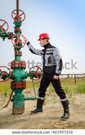 Oilfield worker repairing wellhead valve, wearing red helmet and work clothes with the radio in hos pocket. Oil and gas concept. 