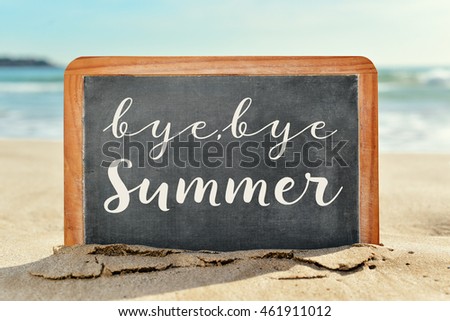 closeup of a chalkboard with the text bye, bye summer written in it, on the sand of a beach