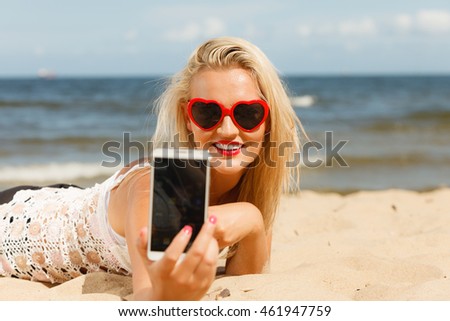 Technology and summer. Woman in red heart shaped sunglasses texting on mobile phone, using smartphone reading sms or taking photo of herself on beach