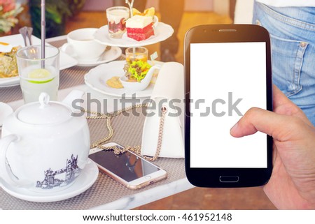 hand holding smartphone with delicious afternoon tea ceremony with snacks in restaurant background.