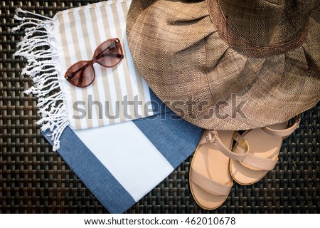 Concept of flat lay summer accessories of white, blue and beige Turkish towel, sunglasses and straw hat on rattan lounger with blue swimming pool as background.