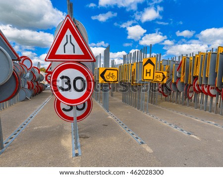 Bottleneck road narrowing sign and thirty speed limit sign among other rows of traffic signs waiting to be hired in road construction projects