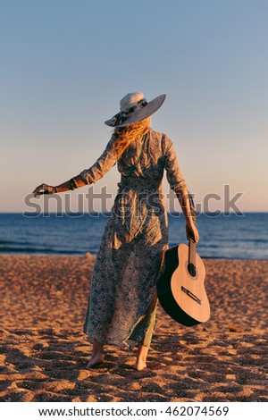 Back view of beautiful elegant lady carrying guitar on beach, sunny blue sky outdoors background