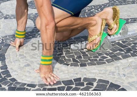 Brazilian athlete wearing flip flops crouching at the start position in running blocks on the tiles of the Ipanema boardwalk in Rio de Janeiro, Brazil