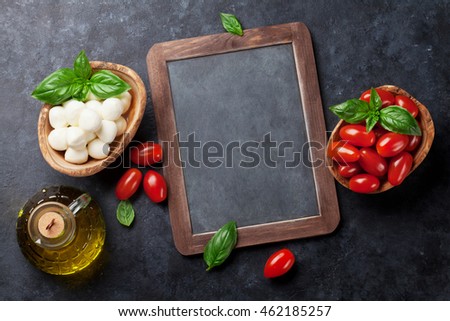 Mozzarella cheese, tomatoes and basil herb leaves over stone table. Blackboard for your text. Top view with copy space