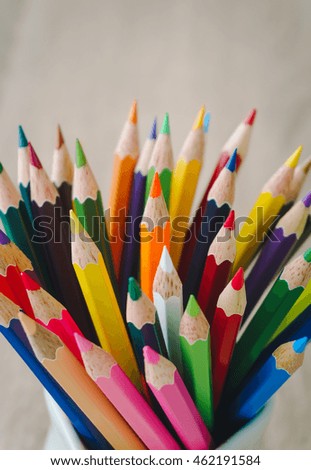 Stack of colored pencils in a glass on wooden background.