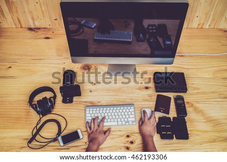 Top view office computer PC camera, mobile phone, headphone,sound recorder,passport,memory card,keyboard and mouse on wooden desk, Asian women hands photo editor working on computer in vintage tone