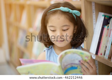 Little Asian child reading a book on the library
