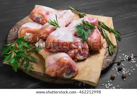 Chicken raw meat shin, drumsticks on wooden cutting board round, spices for cooking chicken drumsticks rosemary, dill, parsley, pepper and salt on dark black background Royalty-Free Stock Photo #462212998