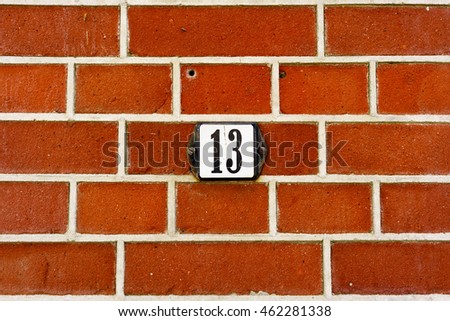 House number thirteen (13) on a red brick wall