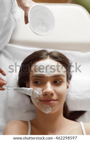 Facial Beauty Treatment. Closeup Of Beautiful Smiling Woman Getting Mask At Spa Salon. Cosmetologist Applying Cosmetic Mask With Brush On Female Face Indoors. Skin Care Concept. High Resolution Image