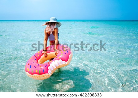 Woman swimming with inflatable donut on the beach in summer sunny day