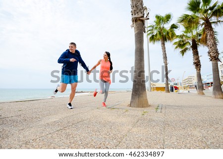 Portrait of happy young couple running together, ocean beach embankment outdoors background