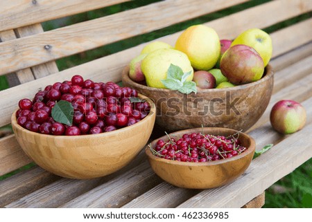 Apples, cherries, red currants lying on a wooden bench in a wooden dish