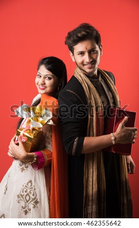 Indian good looking young brother and sister celebrating Raksha Bandhan / Rakhi  festival or on Bhai dooj/Bhau-Beej with Poja Thali, sweets, gifts or taking selfie pictures - Season's Greeting Card