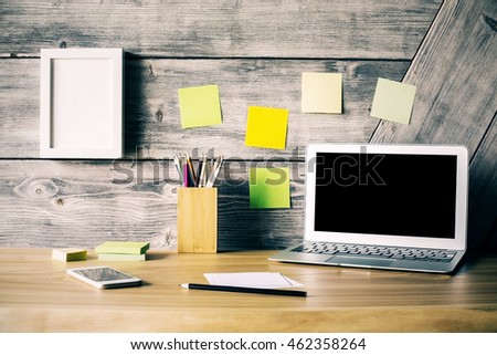 Creative designer desktop with blank laptop screen, picture frame, smartphone, stickers and other stationery items. Mock up
