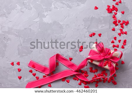 Festive gift box and many little  decorative red hearts on textured grey background. Flat lay with copy space.