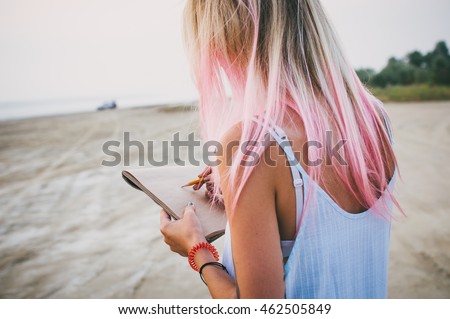 Young hipster woman with pink hair drawing with pencil at the coast