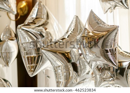 Balloons in the form of silver stars hang before a white curtain