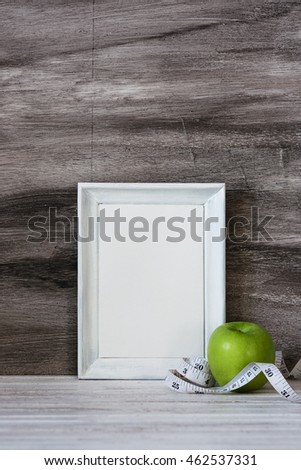 Empty wooden frame for motivation quotes and green apple on the grey wooden background. Fitness concept with text space.