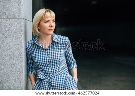 Beautiful blonde girl  in a checkered blue and white dress leaning on the wall.  business woman concept