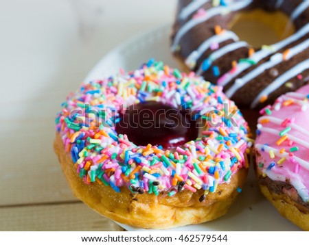 Picture of assorted donuts on white plate with chocolate frosted, pink glazed and sprinkles donuts.