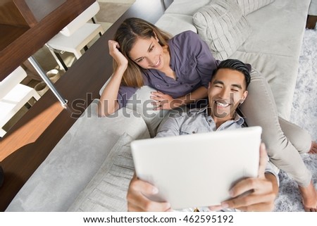 Couple on sitting room sofa taking selfie with digital tablet