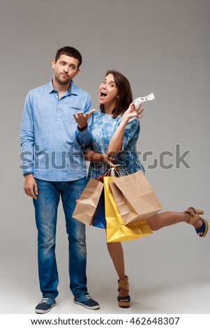Young woman holding purchases, taking last money from man.