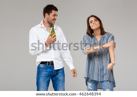 Young woman quarreling, angering with drunk husband over grey background.