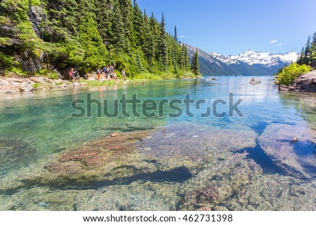 Garibaldi provincial park and lake with turquose water on a sunny day. Snow mountain at the background. Hikers on the trail taking pictures and enjoining the view.