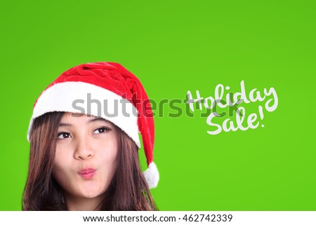 Happy face closeup of pretty girl in Santa's hat, looking at Holiday Sale text over green background design for Christmas season