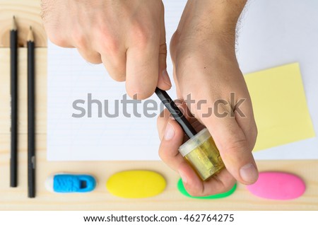 Top view of man's hands sharpening pencil on wooden desktop with blank white paper sheet