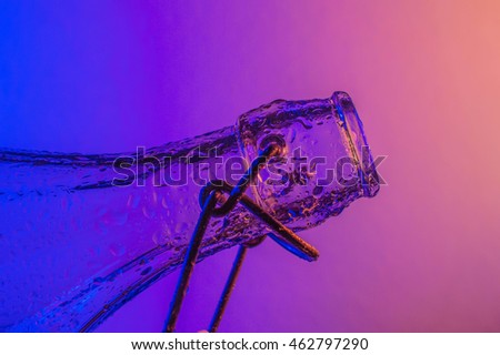 Bottle with droplets with color (blue and yellow) lights in background