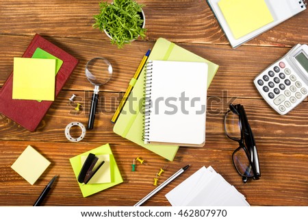 Office table desk with set of colorful supplies, white blank note pad, magnifying glass, cup, pen, pc, crumpled paper, flower on grunge wooden background. Top view and copy space for text