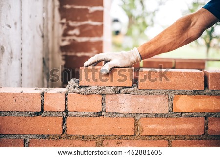 industrial bricklayer worker placing bricks on cement while building exterior walls, industry details Royalty-Free Stock Photo #462881605