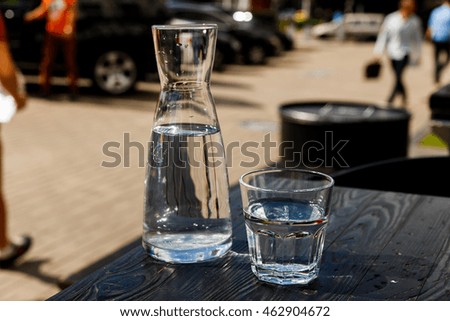 A glass of water and a water-bottle on a black wooden table of a city cafe terrace