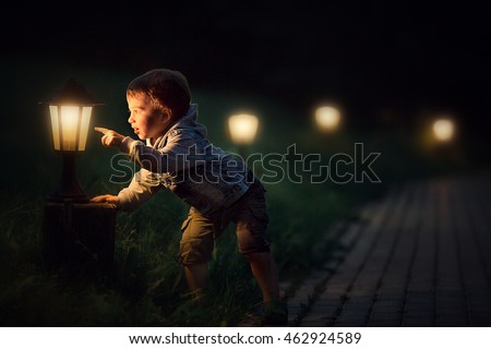 Cute little boy looking and magic light of a lantern in the evening. Image with selective focus and toning