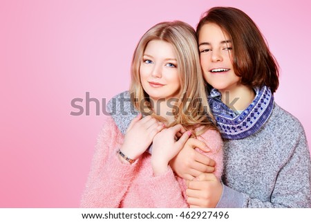 Portrait of happy teenage boy and girl standing together over pink background. Friendship. First love.
