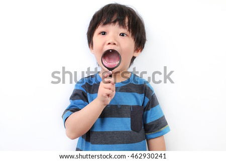 Little Asian boy showing mouth through a magnifying glass, isolated on white