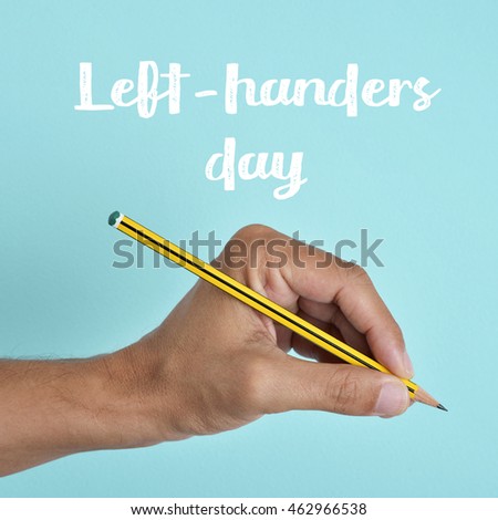 the text left-handers day and the hand of a left-handed man with a pencil, against a blue background Royalty-Free Stock Photo #462966538