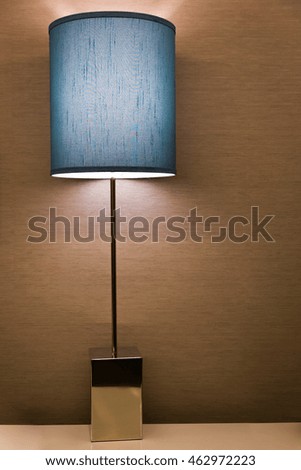 Lit lamp on a white table over a textured wall