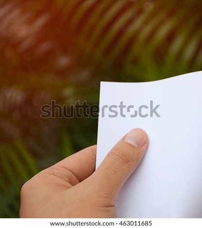 Hand holding white paper with nature background.