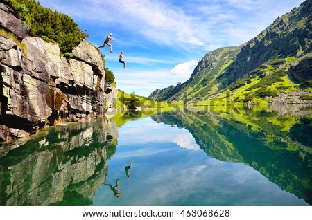 two young people jumping to the water in beautiful mountains nature. Fresh and free scenery from summer vacation Royalty-Free Stock Photo #463068628